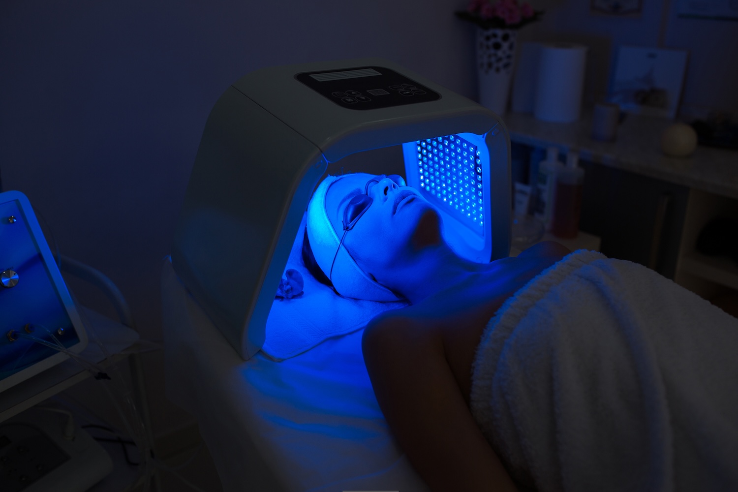 person lying under a blue LED light panel with protective eyewear in a dim treatment room