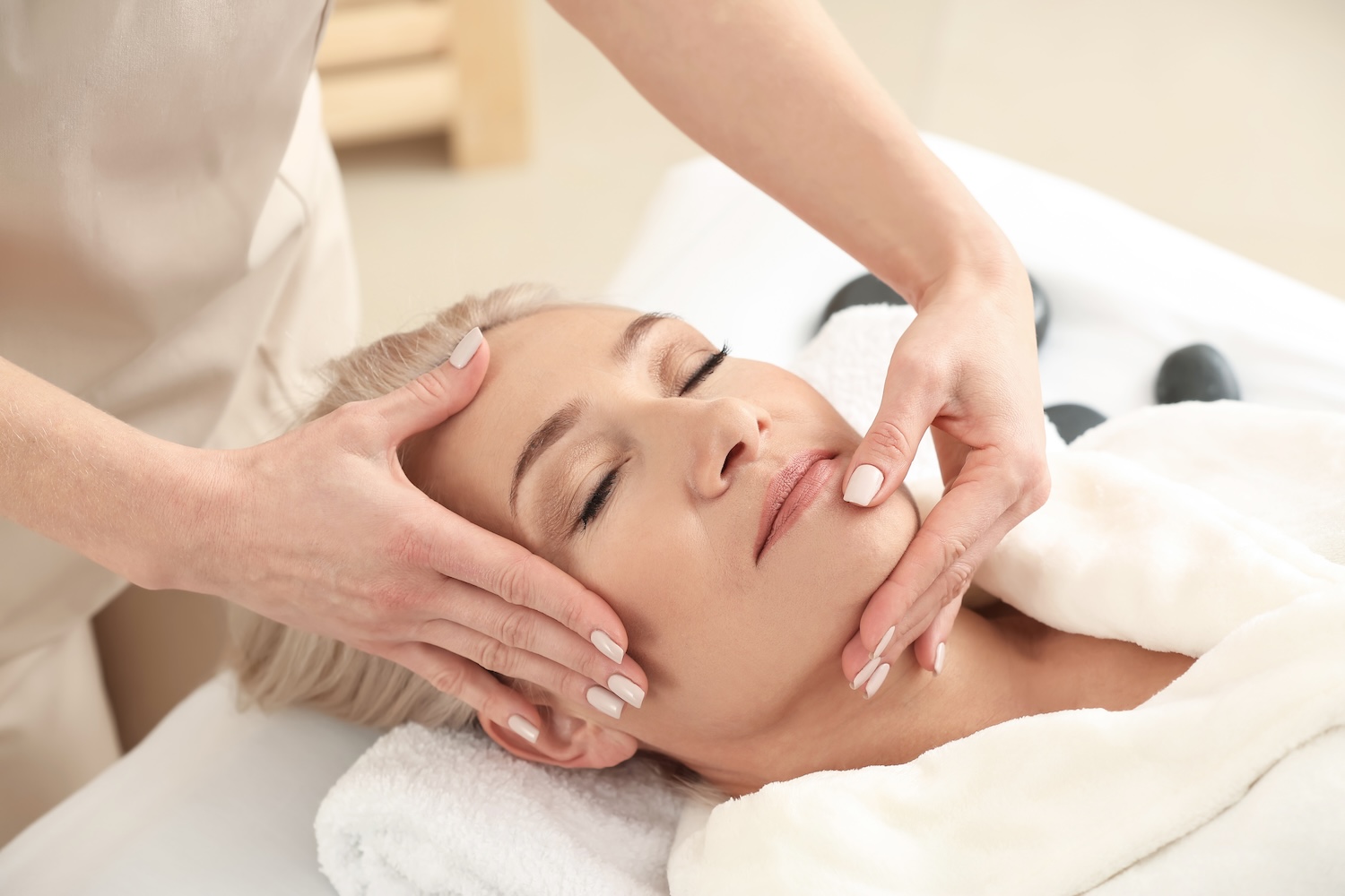 esthetician performing a relaxing anti-aging facial massage on a client with eyes closed