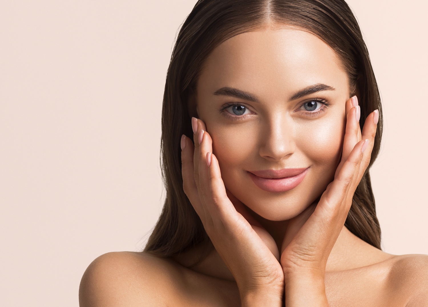 woman with long hair holding both sides of her face with her hands and looking forward against a neutral background