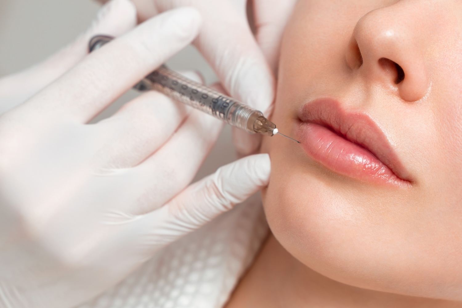 gloved hands holding a syringe near a woman’s upper lip during a close-up injection
