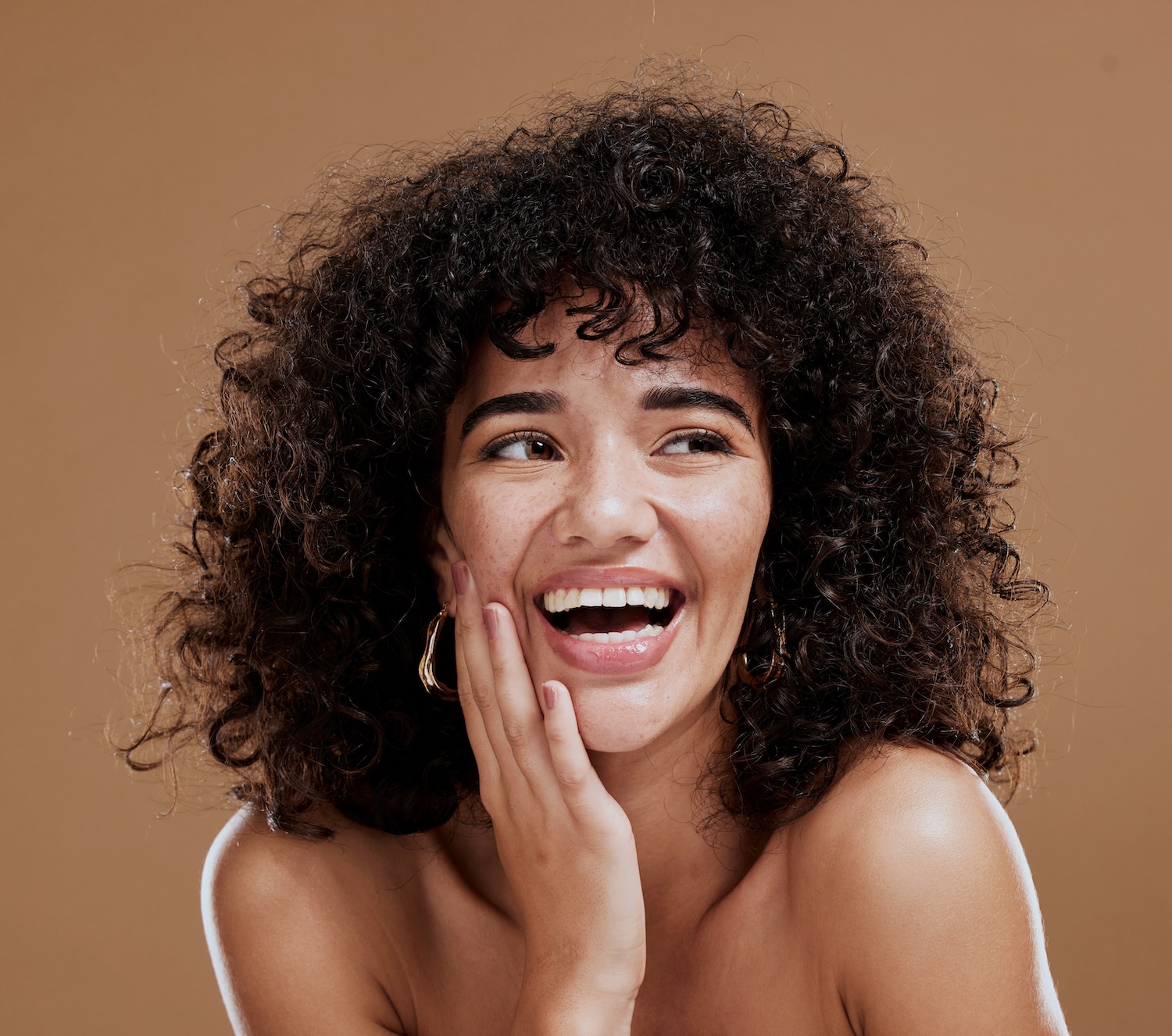 woman smiling with her hand resting on her cheek against a warm brown background