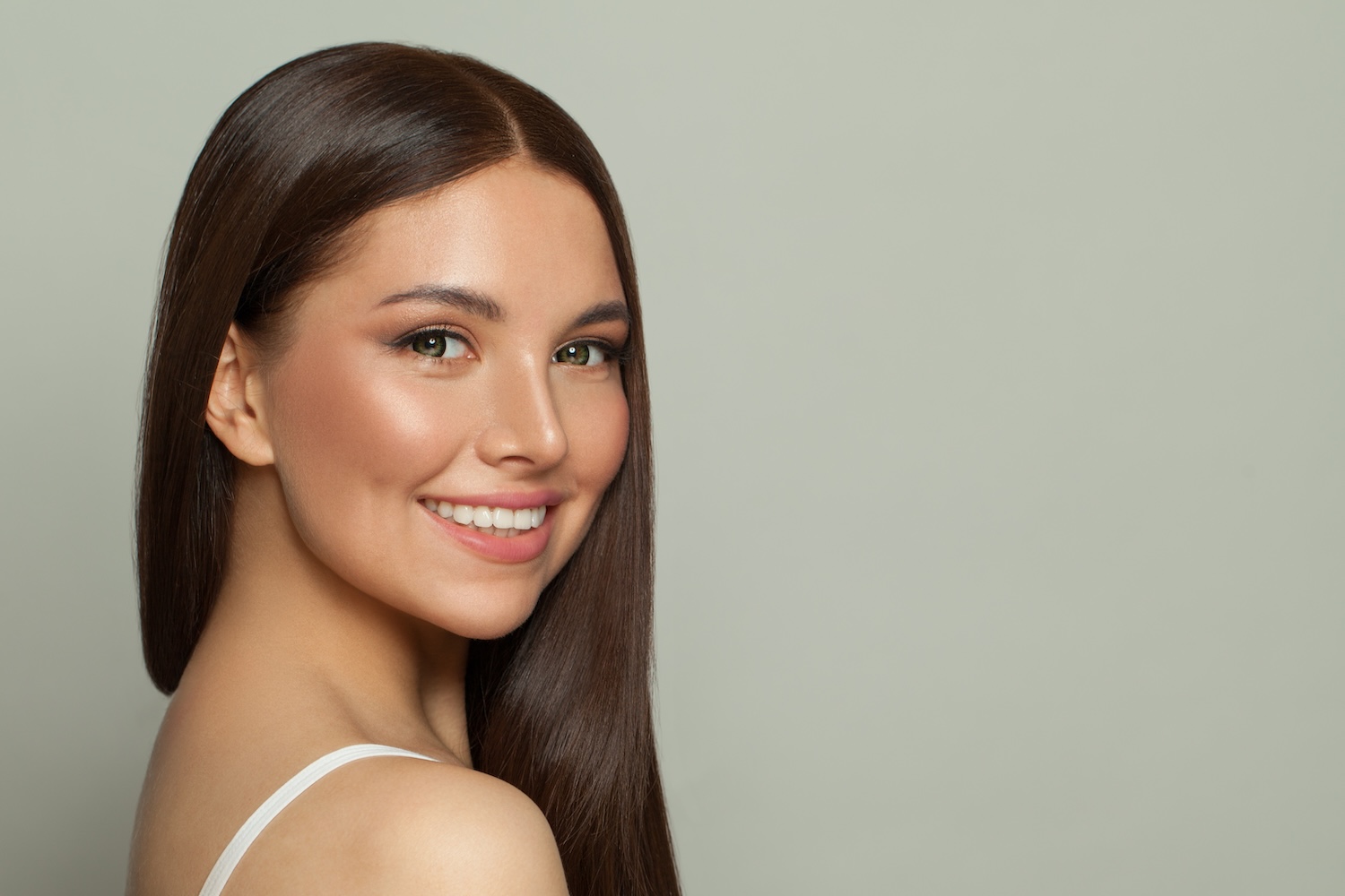 woman smiling while looking over her shoulder against a light background