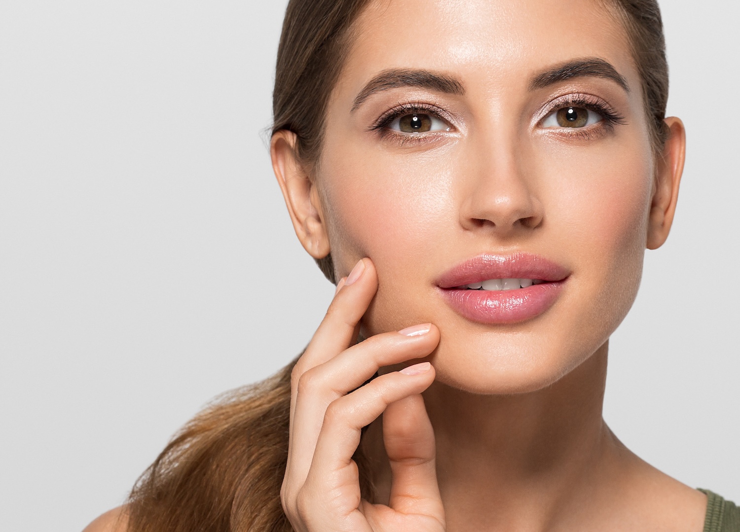 woman touching her cheek with her fingertips while looking ahead against a light background