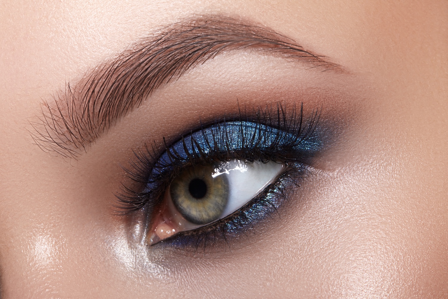 Close-up of a single eye with blue eyeshadow, defined eyelashes, and a natural eyebrow.