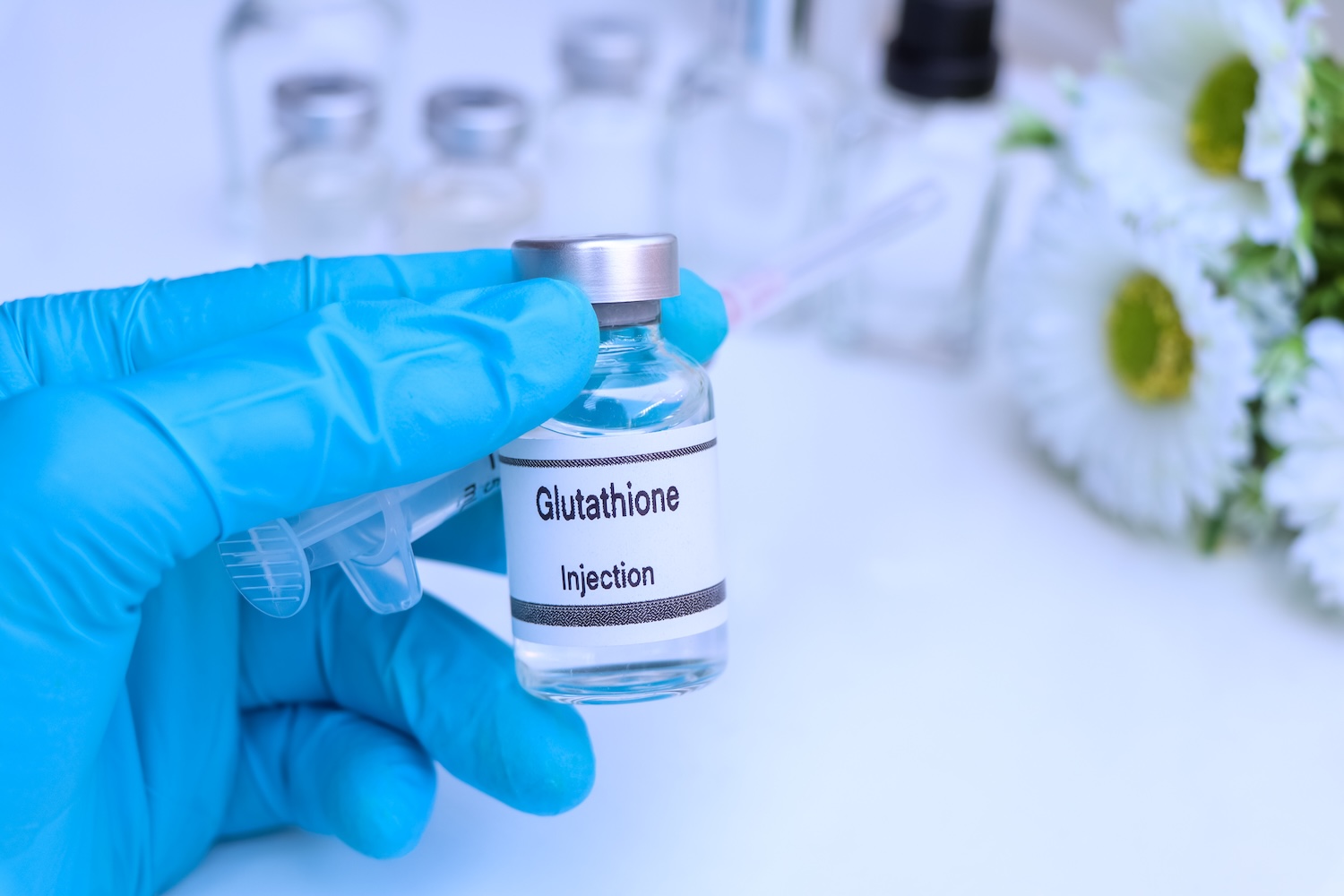 Gloved hand holding a small vial labeled “Glutathione Injection” with a syringe tip visible beside it.