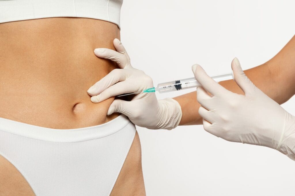 Gloved hands hold a syringe while injecting into the lower abdomen of a person wearing white underwear.