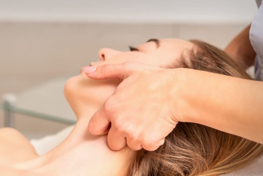hands pressing along a person’s neck as they lie on their back during a massage