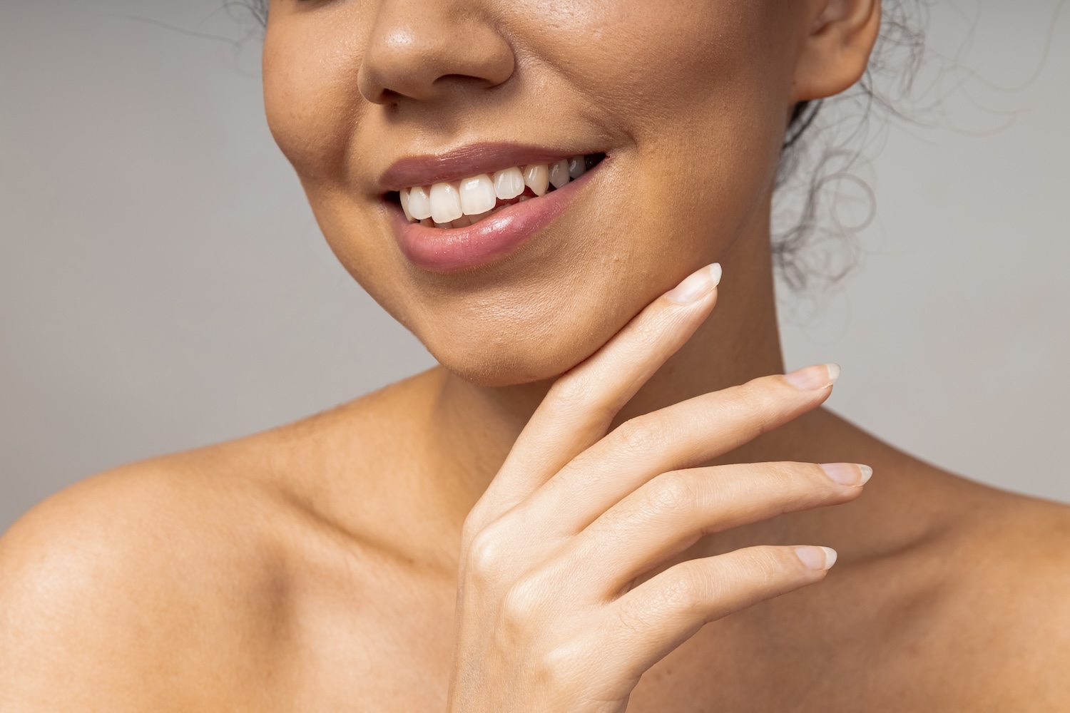 Close-up of a woman smiling, with her hand resting lightly against her chin and neck.