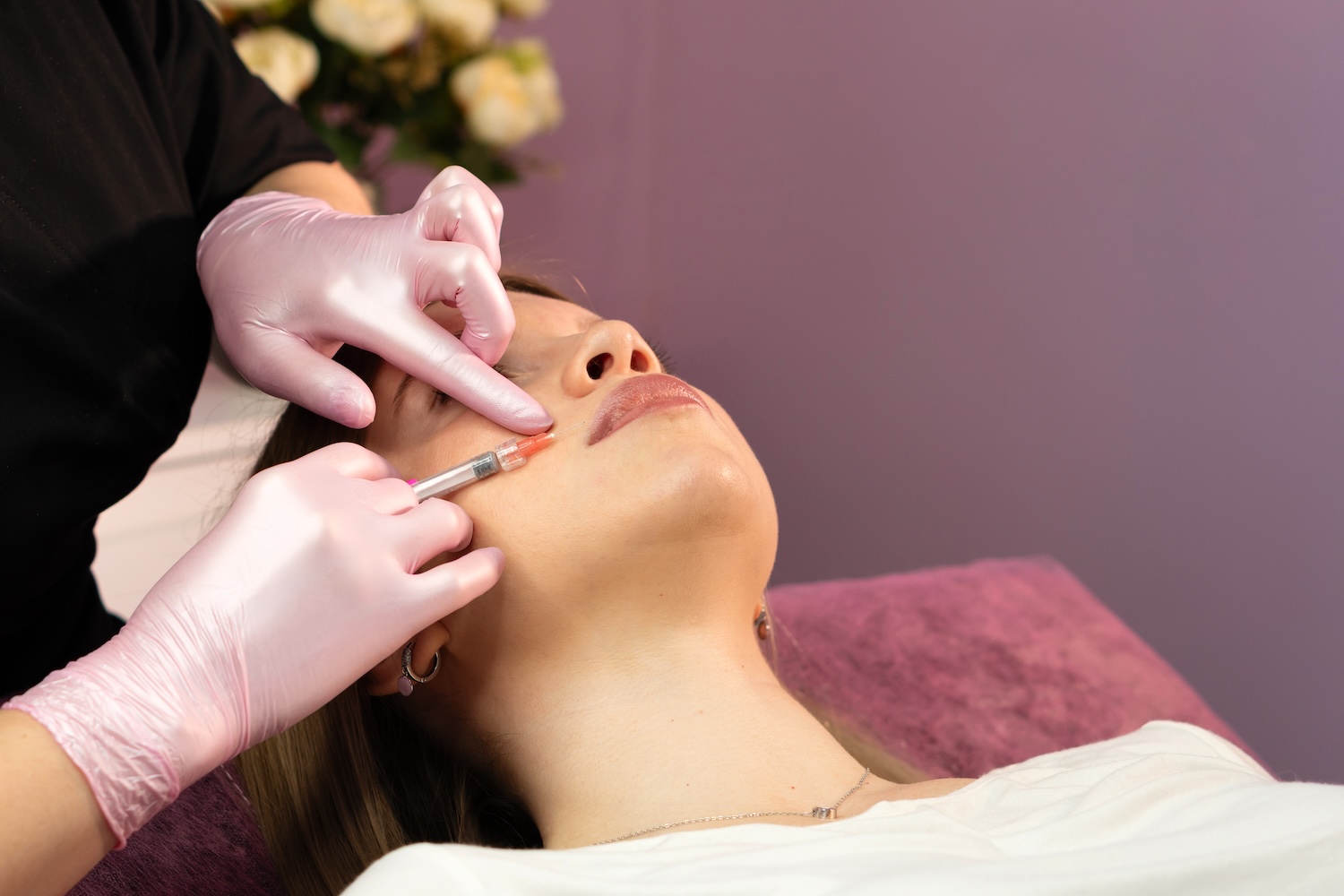 medical professional administering a cheek injection with a syringe while the patient lies back during a cosmetic rejuvenation treatment