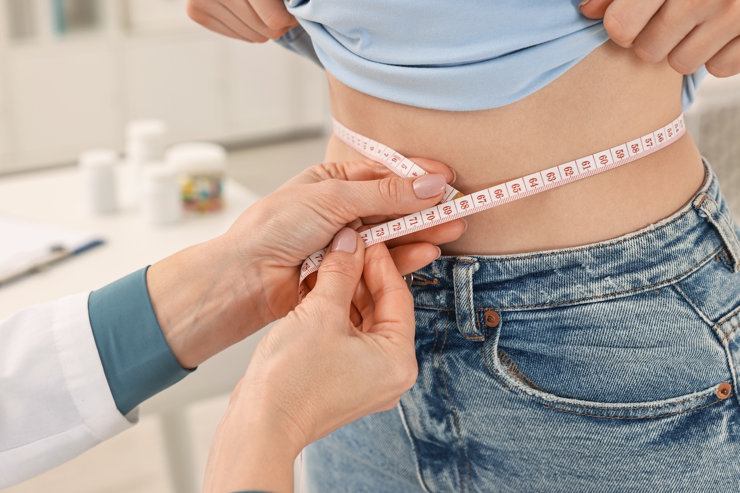 Healthcare professional measuring a patient’s waist with a tape measure during a weight loss or body composition consultation.