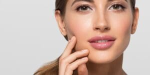 Woman facing forward with her finger resting lightly on her cheek against a neutral background.